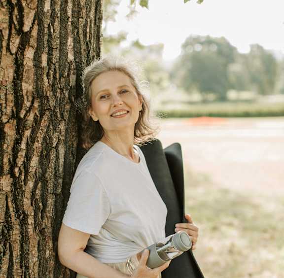 A woman leaning against a tree holding a camera.