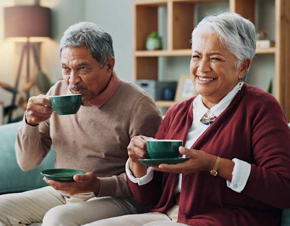 a man and a woman sitting on a couch holding cups of coffee