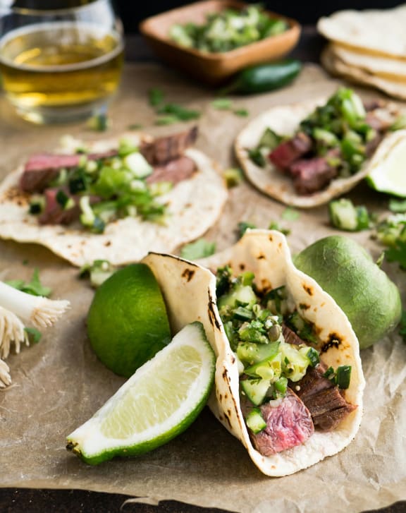 a plate of tacos with meat and avocado and a glass of beer