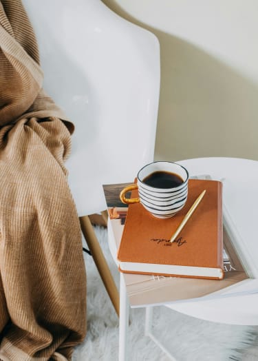 a cup of coffee sitting on top of a book on a chair with a blanket at Bradford Gwinnett Apartments in  Georgia 30071