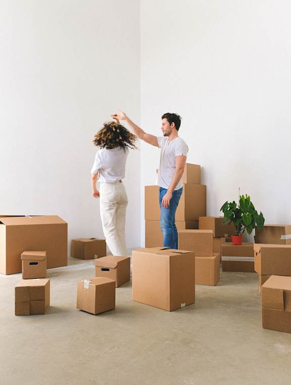 A man and woman dancing in a room surrounded by cardboard boxes.