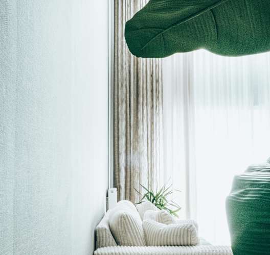a white chair with pillows and a plant in front of a window