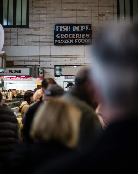 a crowd of people in a grocery store with a sign for fish defrost groceries