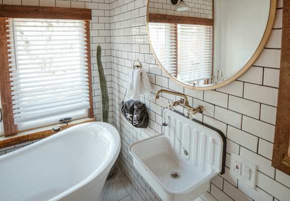 A white sink is mounted on a wall with a round mirror above it.