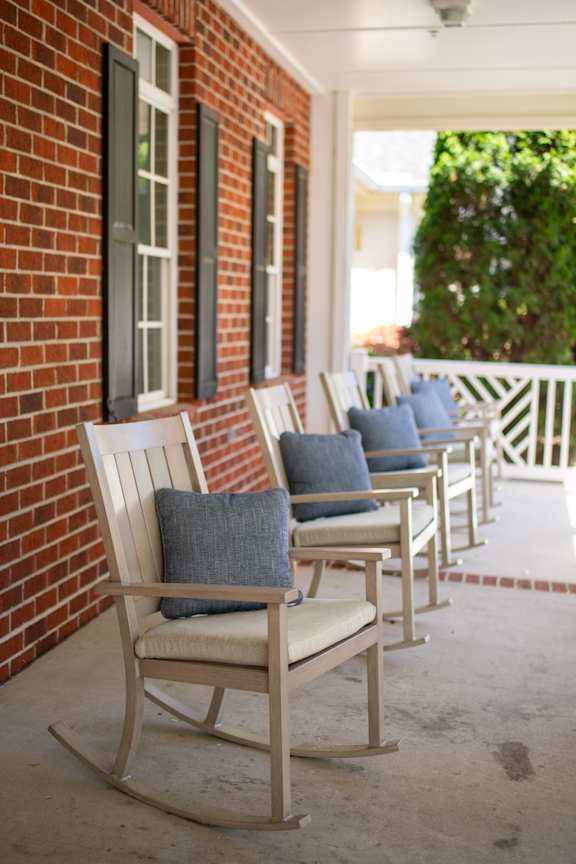 A row of rocking chairs with cushions are lined up on a porch.