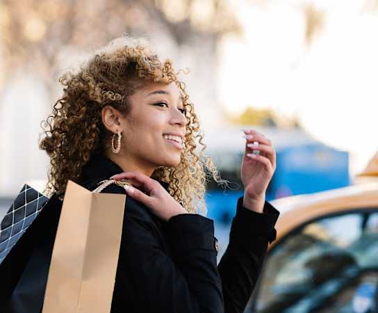 a woman with curly hair holding a shopping bag at The Merc, Waltham, Massachusetts