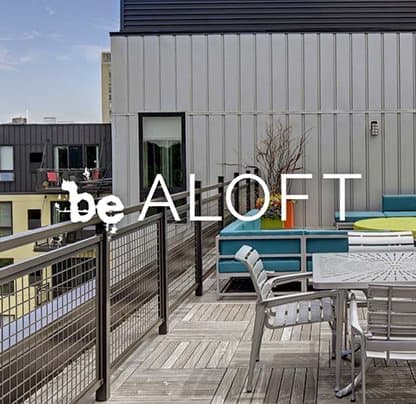 Be ALOFT phrase with background of rooftop patio with chairs, a table, and blue couches at Be @ Axon Green, Minneapolis