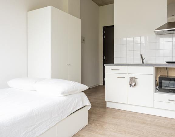 A white bedroom with a bed, a microwave, and a cabinet.