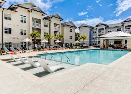 A swimming pool surrounded by lounge chairs and umbrellas in front of apartment buildings.