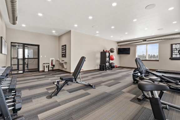 A gym with a variety of equipment including treadmills, weights, and a television.