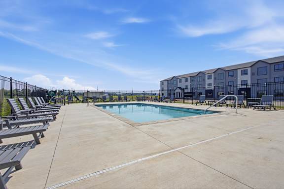 A swimming pool surrounded by lounge chairs and a fence.