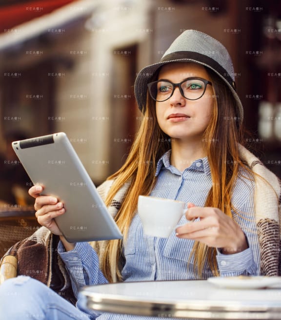 a young woman using a tablet computer and holding a cup of coffee