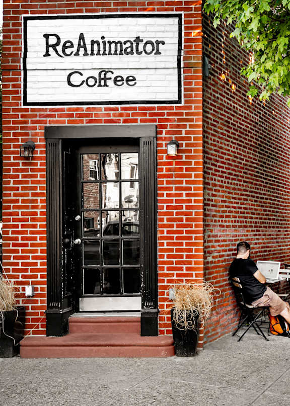 A man is sitting outside of a brick building with a sign that says ReAnimator Coffee.