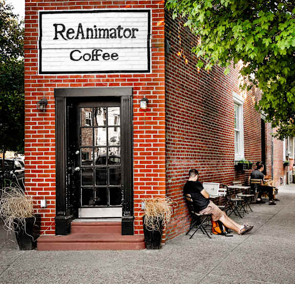 A man is sitting outside of a brick building with a sign that says ReAnimator Coffee.