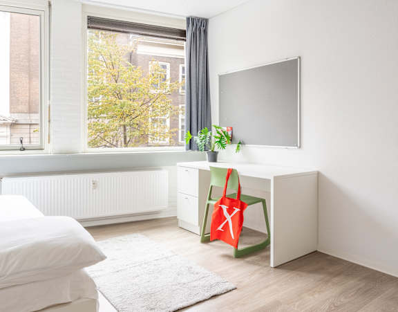 A white bedroom with a bed, desk, and window.