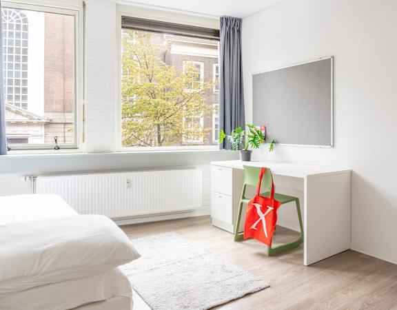 A white bedroom with a bed, desk, and window.