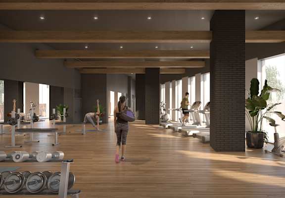A woman is walking through a spacious gym with wooden floors and various exercise equipment.