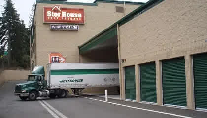 A green semi truck is parked in front of a Stor House self storage facility.