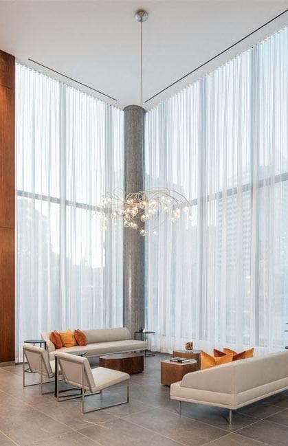 a living room with white curtains and chairs and a chandelier