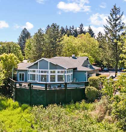 A house with a green fence is surrounded by trees and bushes.