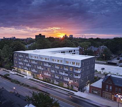 A modern building is lit up at dusk with the sun setting in the background.
