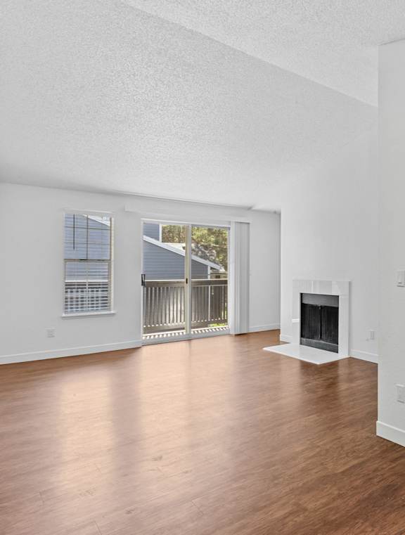 A large empty room with a fireplace and wooden floors.
