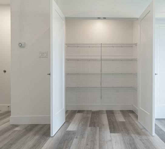 an empty room with white walls and wood flooring and a closet with empty shelves