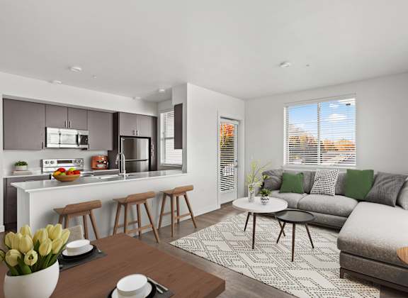 A modern kitchen with a breakfast bar and a living room with a grey couch.