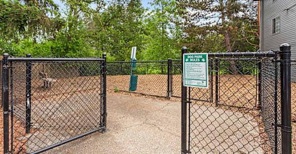 A dog park is enclosed by a black fence and has a sign on it.