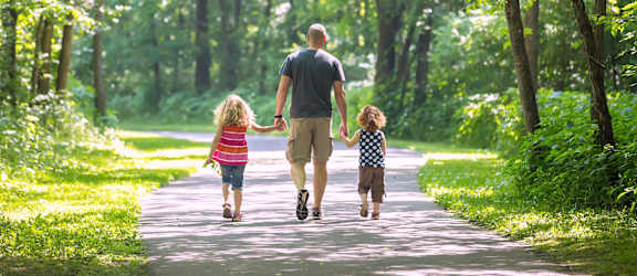 A man and two children are walking down a path in the woods.