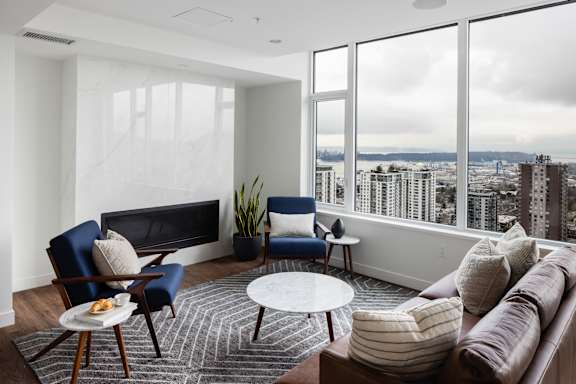 A living room with a brown couch, blue chairs, and a view of the city.