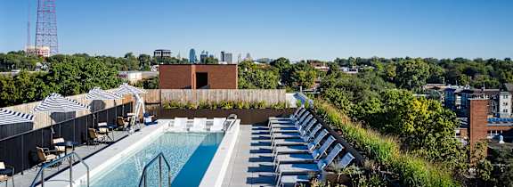 A rooftop pool with sun loungers and a view of the city.