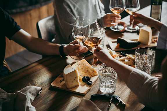 A group of people toasting with glasses of wine at a table with cheese boards.