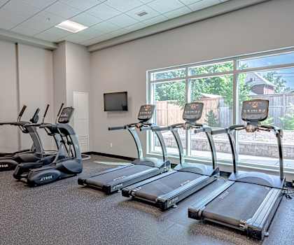 a gym with cardio machines and a large window