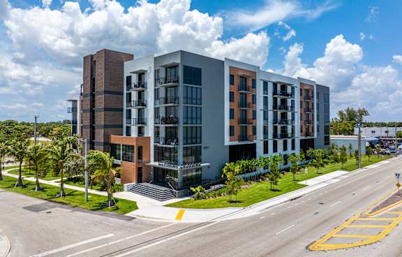 A modern multi-story building with a parking lot in front.