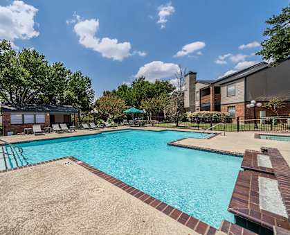 A large swimming pool surrounded by a sandy area and a few trees.