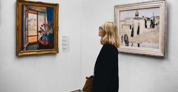 A woman is looking at paintings in a gallery.