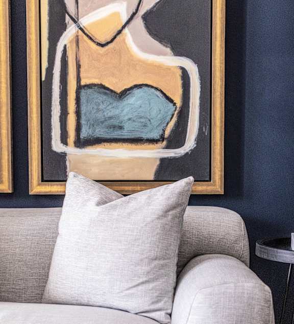A grey couch with a pillow and a painting in the background.