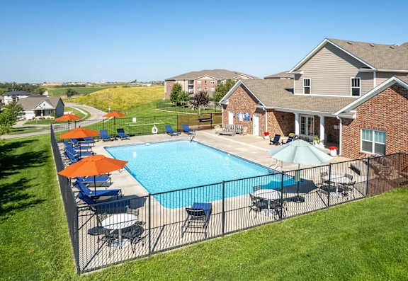 A pool surrounded by a black fence with orange and blue umbrellas.