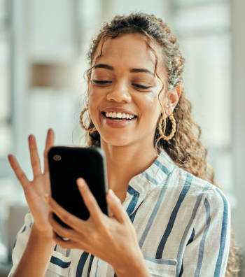 A woman with curly hair is smiling while looking at her phone.