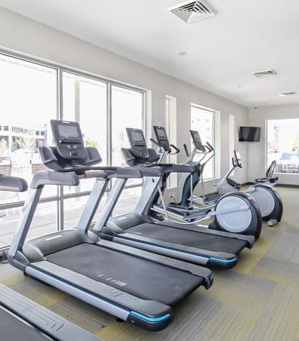 a gym with a row of cardio equipment and windows