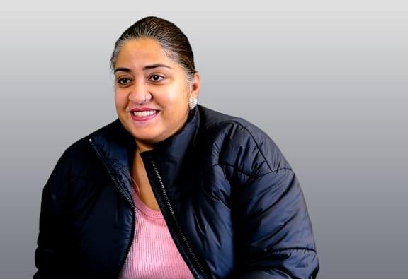 A woman with a ponytail is wearing a black jacket and a pink shirt.