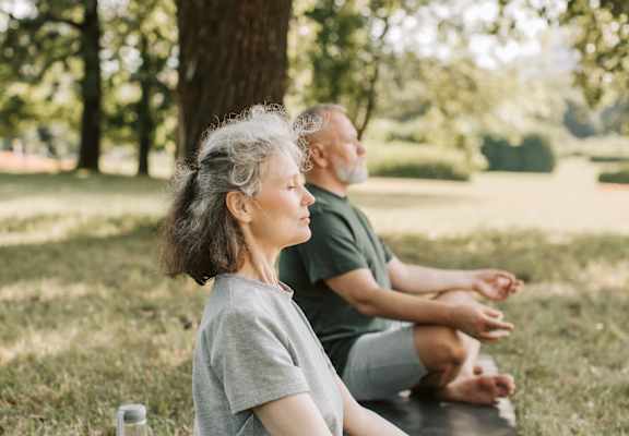 a man and a woman sitting on a yoga mat in a park