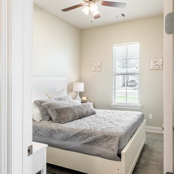 A bedroom with a bed, pillows, a ceiling fan, and a window.