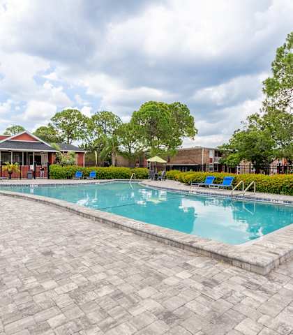 A pool surrounded by a brick patio and a red building in the background.