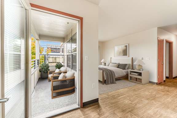 A bedroom with a bed, nightstand, and chair is shown through an open door.