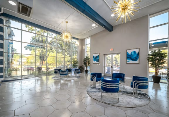 a lobby with blue chairs and large windows and a chandelier