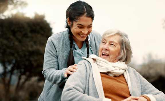 An elderly woman is being comforted by a younger woman in a park.