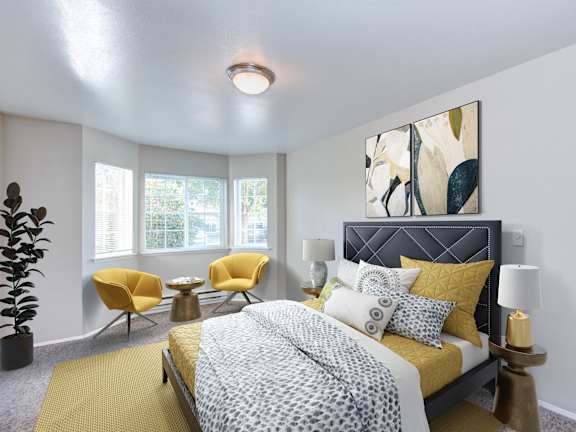 A bedroom with a bed, two chairs, and a potted plant.
