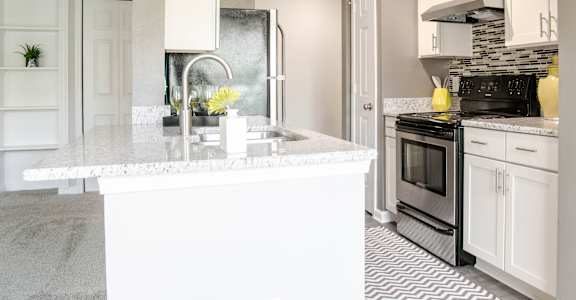 A kitchen with a marble countertop and a black refrigerator.